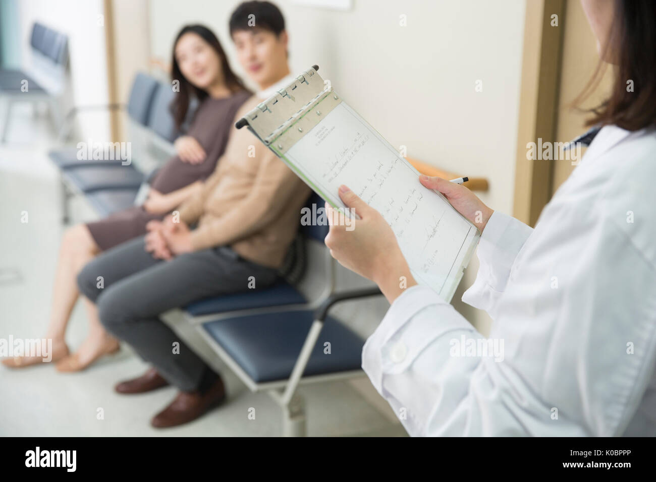 Medico con grafico e incinta giovane seduto alla sala di attesa Foto Stock