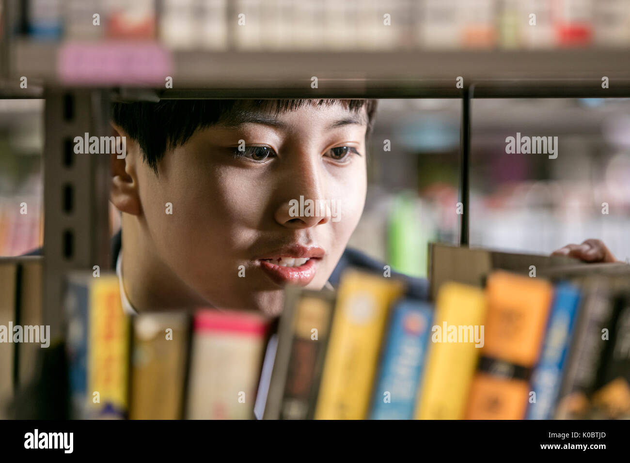 La faccia del ragazzo scuola cercando un libro in biblioteca Foto Stock