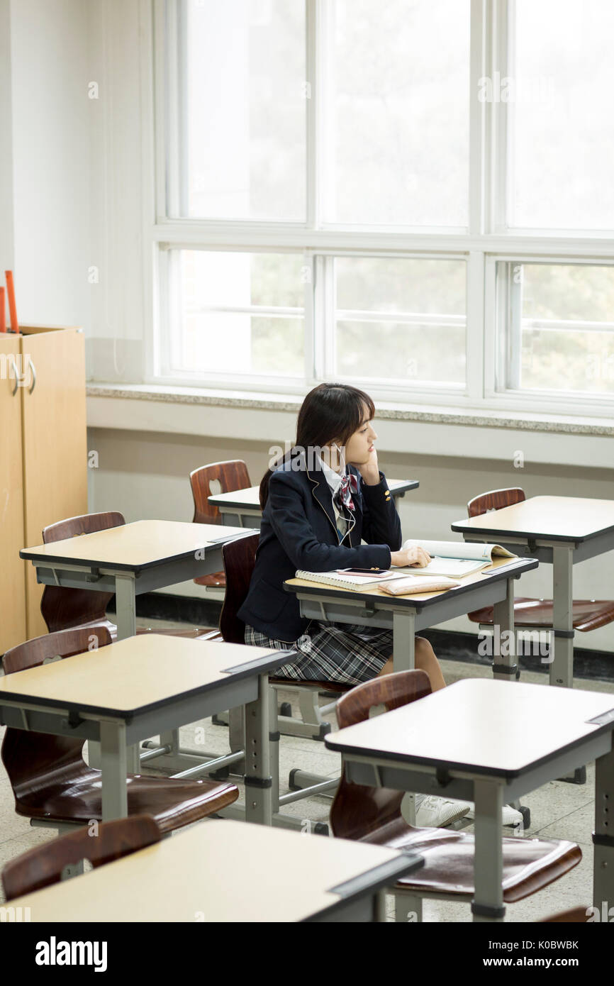 Vista laterale della scuola solitaria ragazza seduta in aula Foto Stock