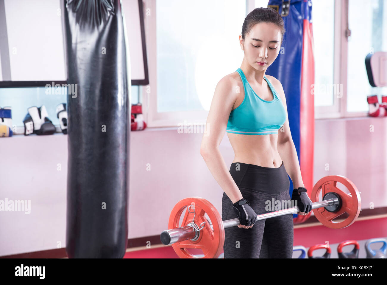 Giovane donna in azienda di abbigliamento sportivo di pesi guardando giù in palestra Foto Stock
