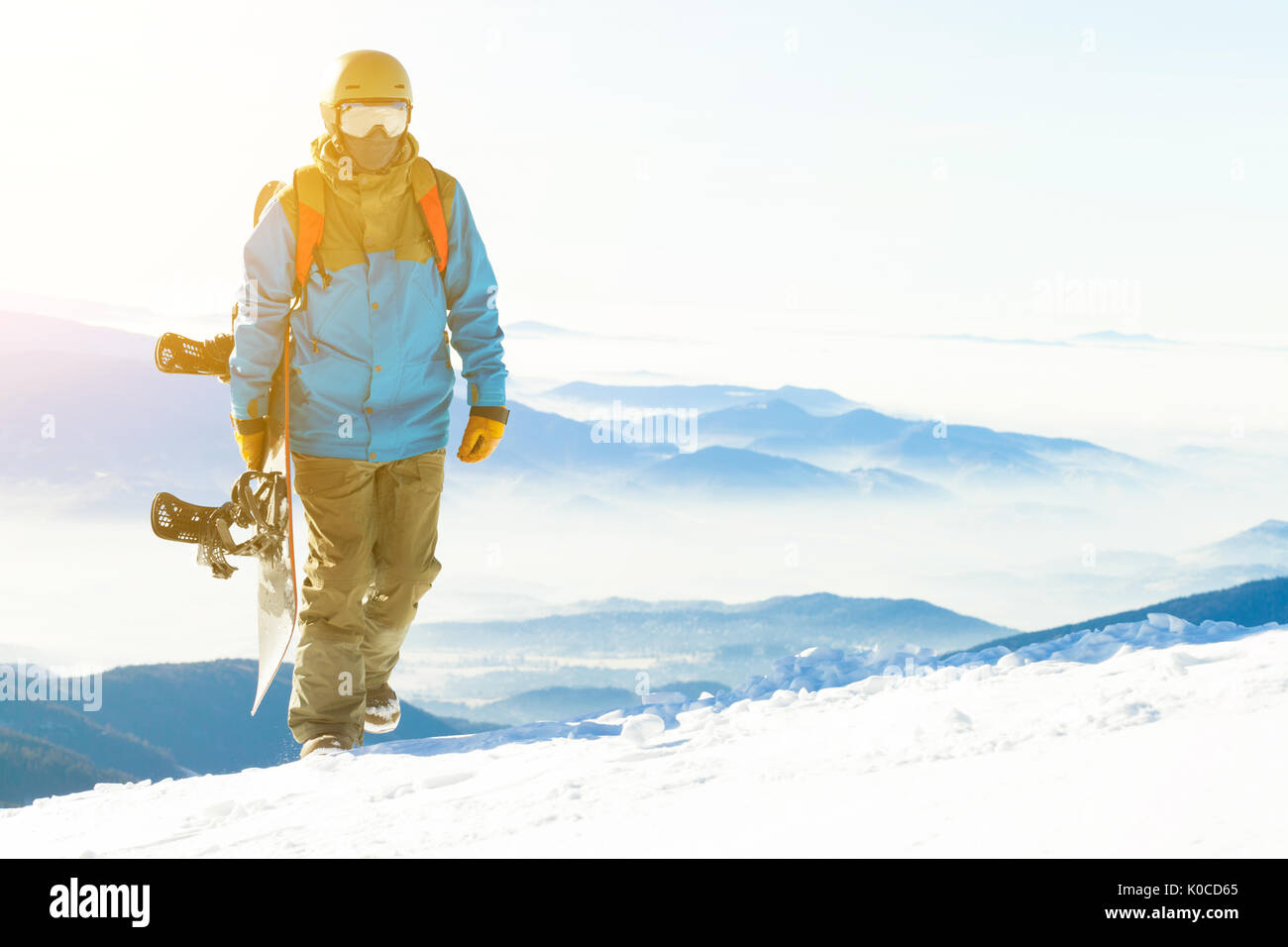 Snowboarder con sun dietro di lui a piedi fino alla montagna snowboard tenendo a portata di mano Foto Stock