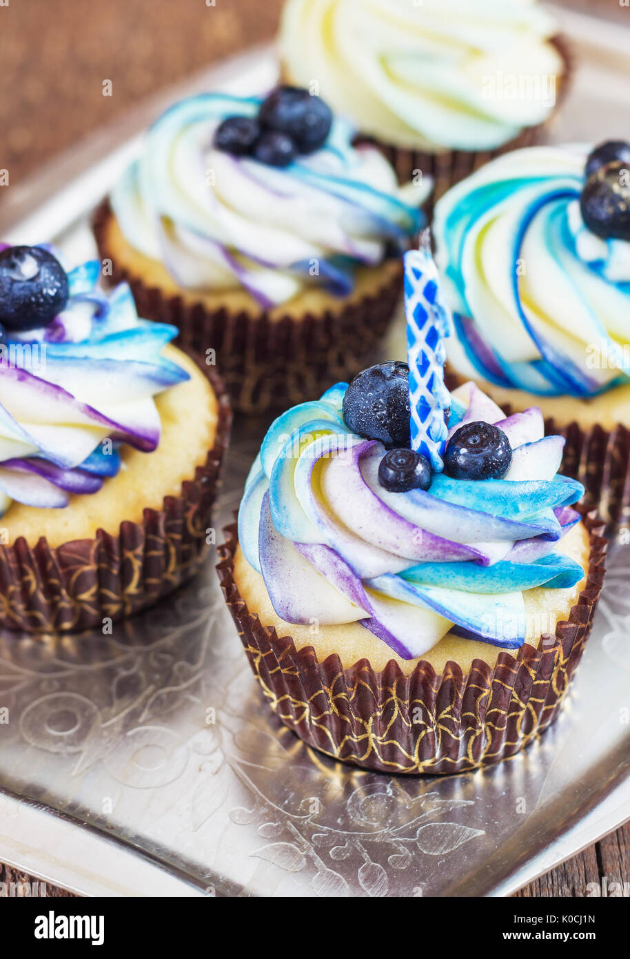 Festive cupcake su uno sfondo di legno con un luminoso color crema e mirtillo con una candela in stile rustico. Foto Stock