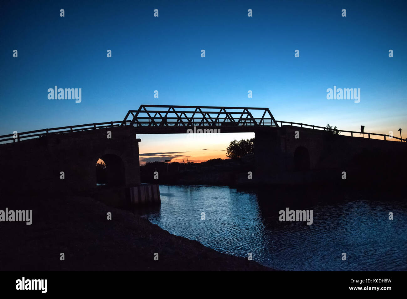 Ponte in legno sul canal al tramonto contro il cielo chiaro Foto Stock