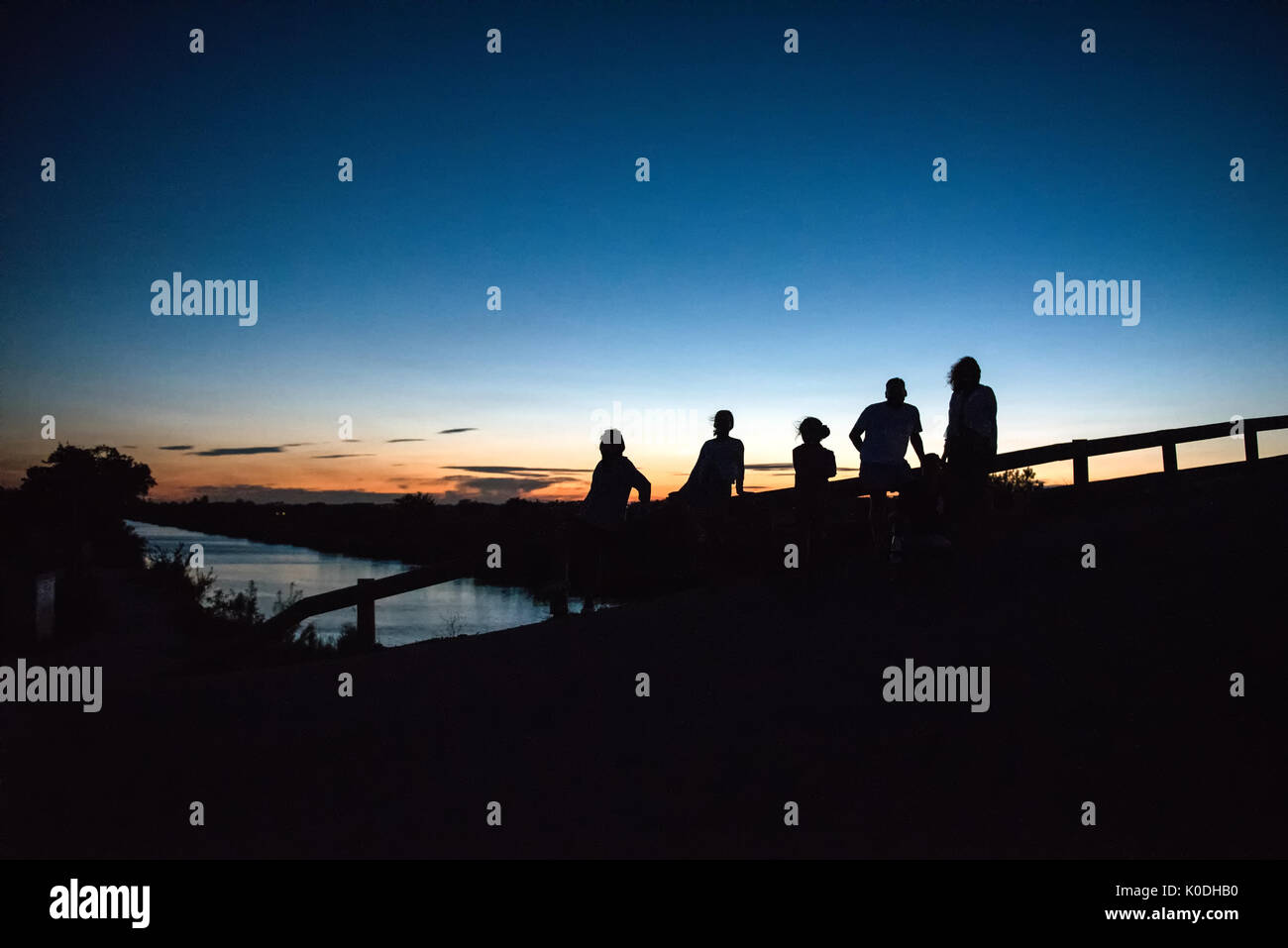 Sagome di cinque persone in piedi sul ponte di legno al tramonto contro il cielo chiaro Foto Stock