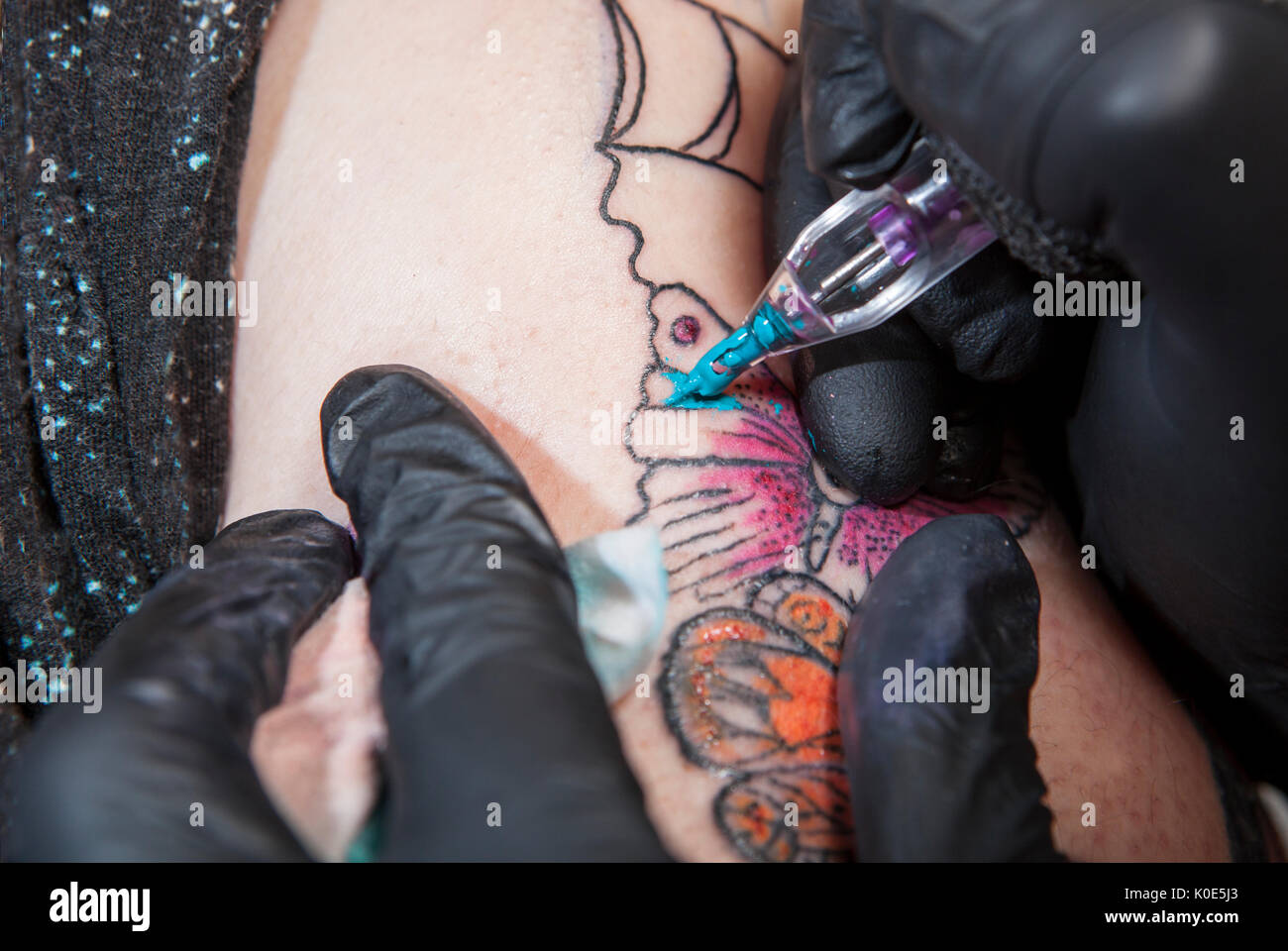 Tattoo Artist tattoo si applica al braccio. Ella è in fase di riempimento con il colore blu chiaro il tatuaggio Foto Stock