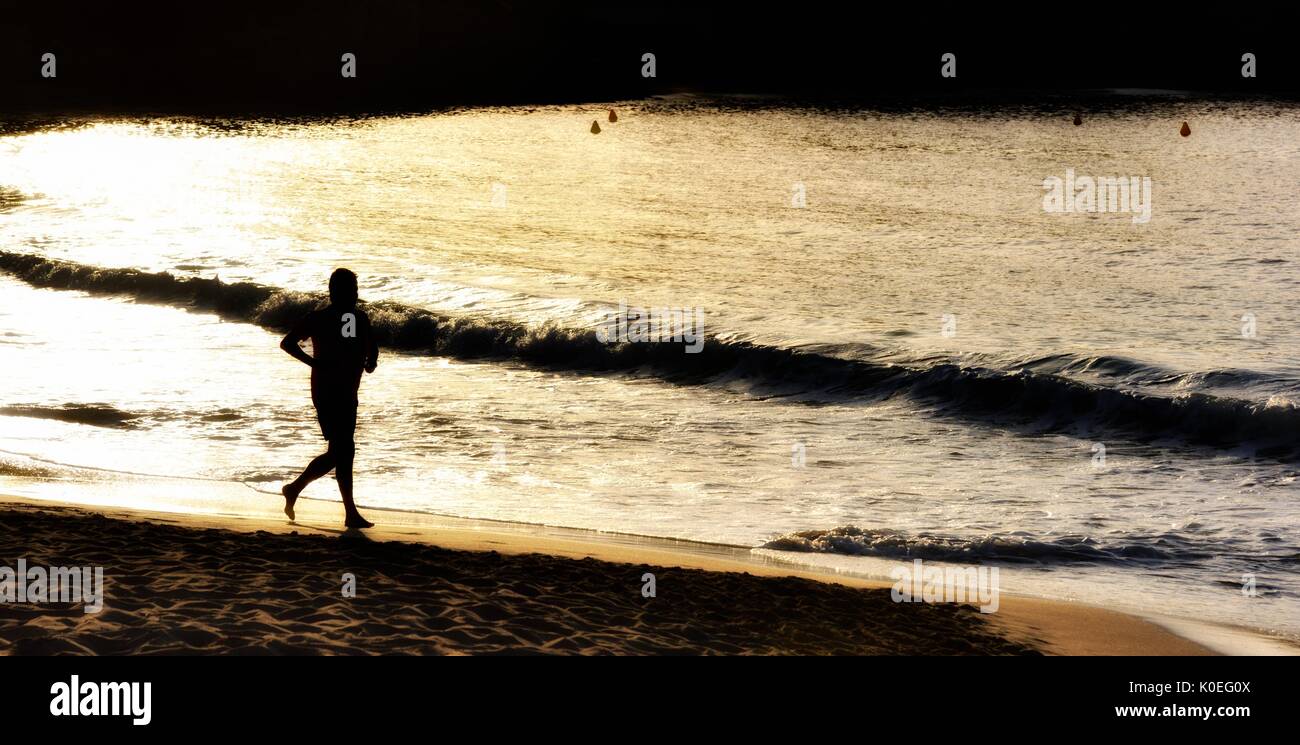 Uomo che corre lungo una spiaggia al tramonto Menorca Minorca Foto Stock