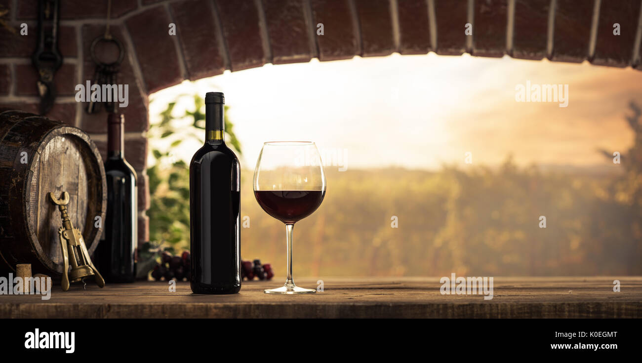 Vino rosso degustazione in cantina: wineglass e bottiglie accanto alla finestra e vista panoramica dei vigneti al tramonto Foto Stock