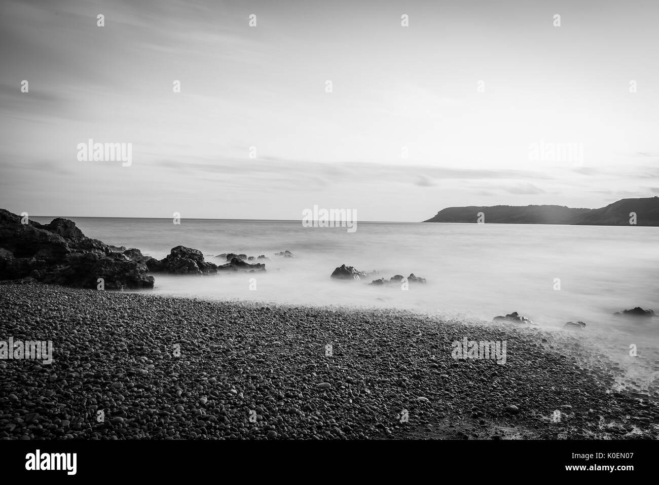 Un costiere esposizione lunga scena con il sole, il mare di sabbia e roccia in bianco e nero, nei pressi di Caswell Bay sulla Penisola di Gower in Galles, Regno Unito Foto Stock