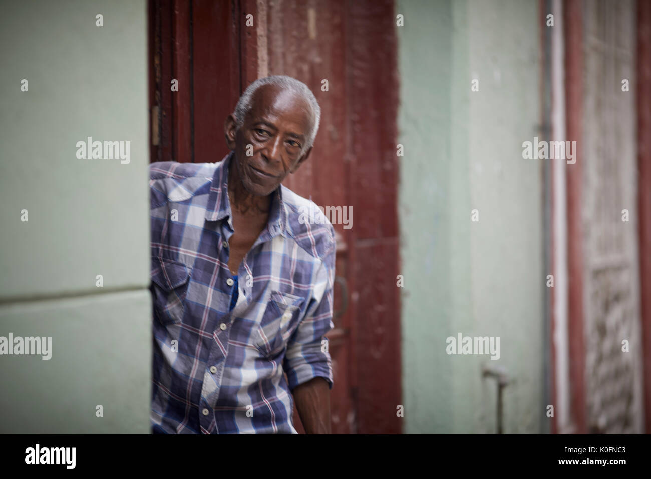Cubano, Cuba, capitale, Havana tipica strada stretta con gli appartamenti una coppia maschio nero guarda fuori forma una porta Foto Stock