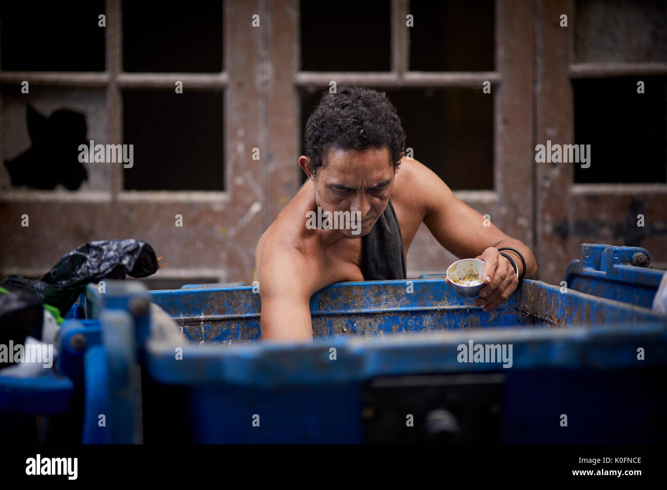 Cubano, Cuba, capitale, Havana un uomo cerca attraverso la spazzatura in un grande contenitore in strada Foto Stock