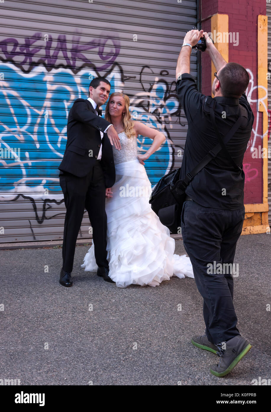 Un fotografo cattura la sposa & in posa e raffreddare agendo contro uno sfondo di graffiti. Foto Stock