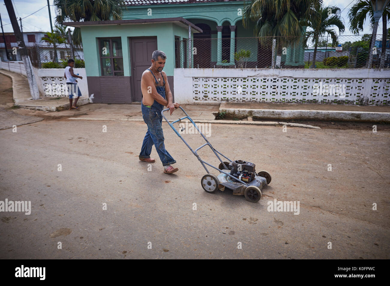 Cubano, Cuba, Cardenas, uomo spingendo un tosaerba attraverso le strade di un povero villaggio Foto Stock
