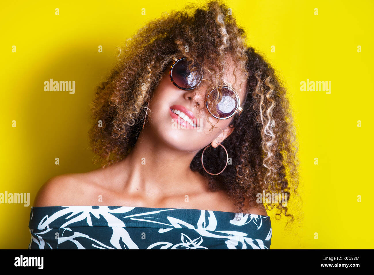 Ritratto in interni di un giovane afro american donna in occhiali da sole. Sfondo giallo. Stile di vita. Foto Stock