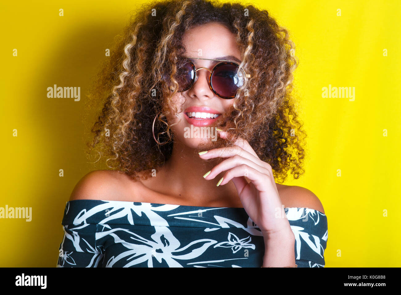 Ritratto in interni di un giovane afro american donna in occhiali da sole. Sfondo giallo. Stile di vita. Foto Stock