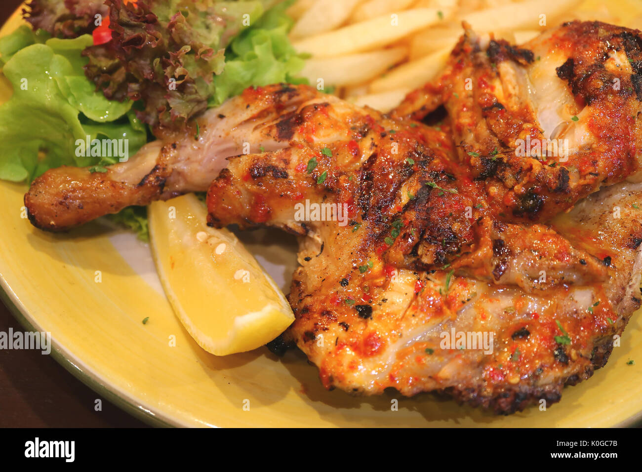 Chiuso fino alla griglia di fiamma di pollo piccante con un pezzo di limone e insalata verde Foto Stock