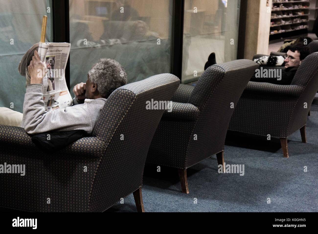Uno studente e un professore, che legge un giornale, siedono in sedie a livello M (principale) della Milton S. Eisenhower Library nel campus Homewood della Johns Hopkins University di Baltimora, Maryland, 2014. Cortesia Eric Chen. Foto Stock