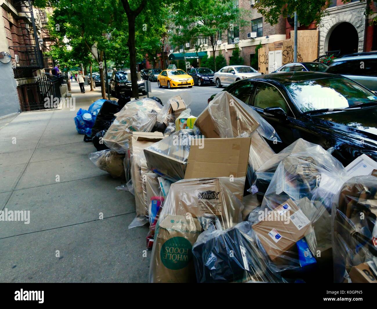 Insaccò, Manhattan garbage posto a lato del marciapiede per regolare del raccoglitore di rifiuti come giallo cabina passa da. Upper Eastside. New York, NY, STATI UNITI D'AMERICA. Foto Stock