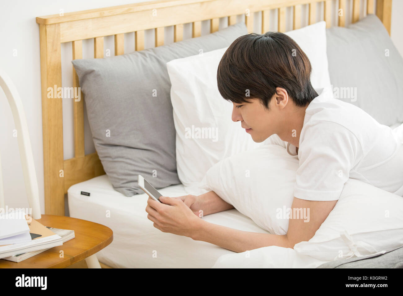 Vista laterale verticale del singolo uomo utilizza lo smartphone sdraiato a faccia in giù sul letto Foto Stock