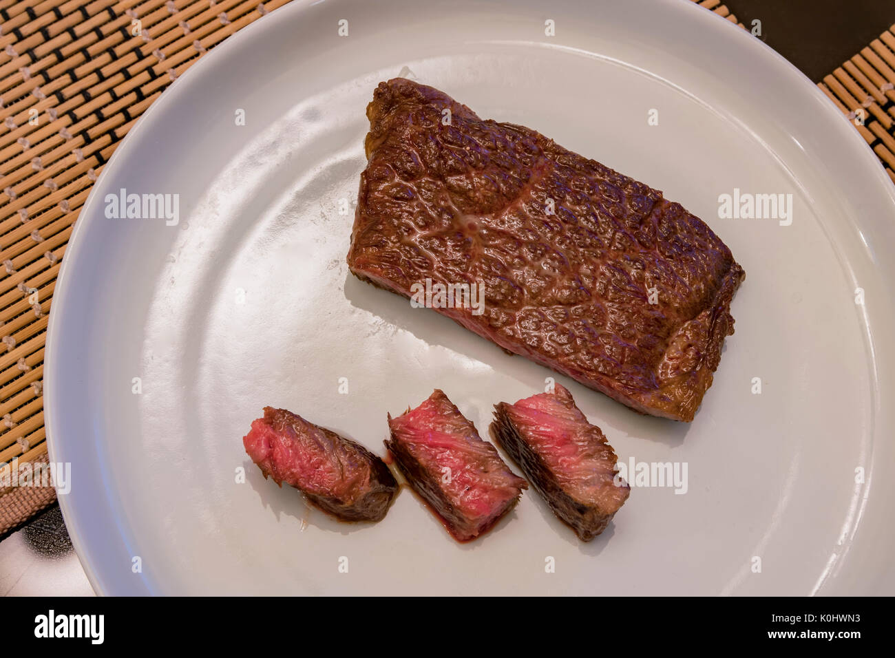 Mezzo raro cotte Wagyu carni bovine a sedersi su una piastra bianca Foto Stock
