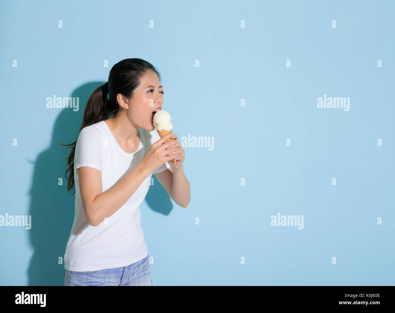 Bella donna graziosa doloroso mangiare il gelato sfida dente sensibile malattia permanente sulla parete blu di sfondo e guardando all'area vuota. Foto Stock