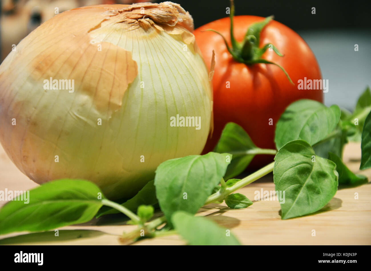 Un giallo cipolla, pomodoro e stelo di basilico su un tagliere in cucina come ingredienti pronta per essere tagliata per fare un sugo per la pasta. Foto Stock