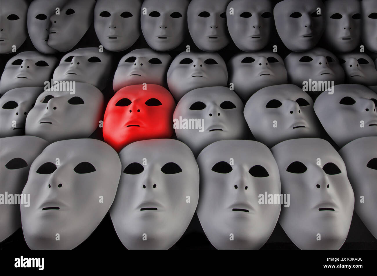 Rosso brillante la maschera per il viso tra le tante maschere bianche su  sfondo nero. Da soli in mezzo alla folla concept Foto stock - Alamy