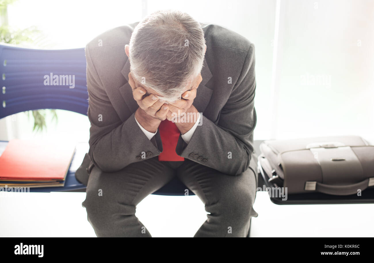 Imprenditore disperato in sala d'attesa con testa in mani, egli è in attesa di un colloquio di lavoro; la disoccupazione e il fallimento aziendale concept Foto Stock