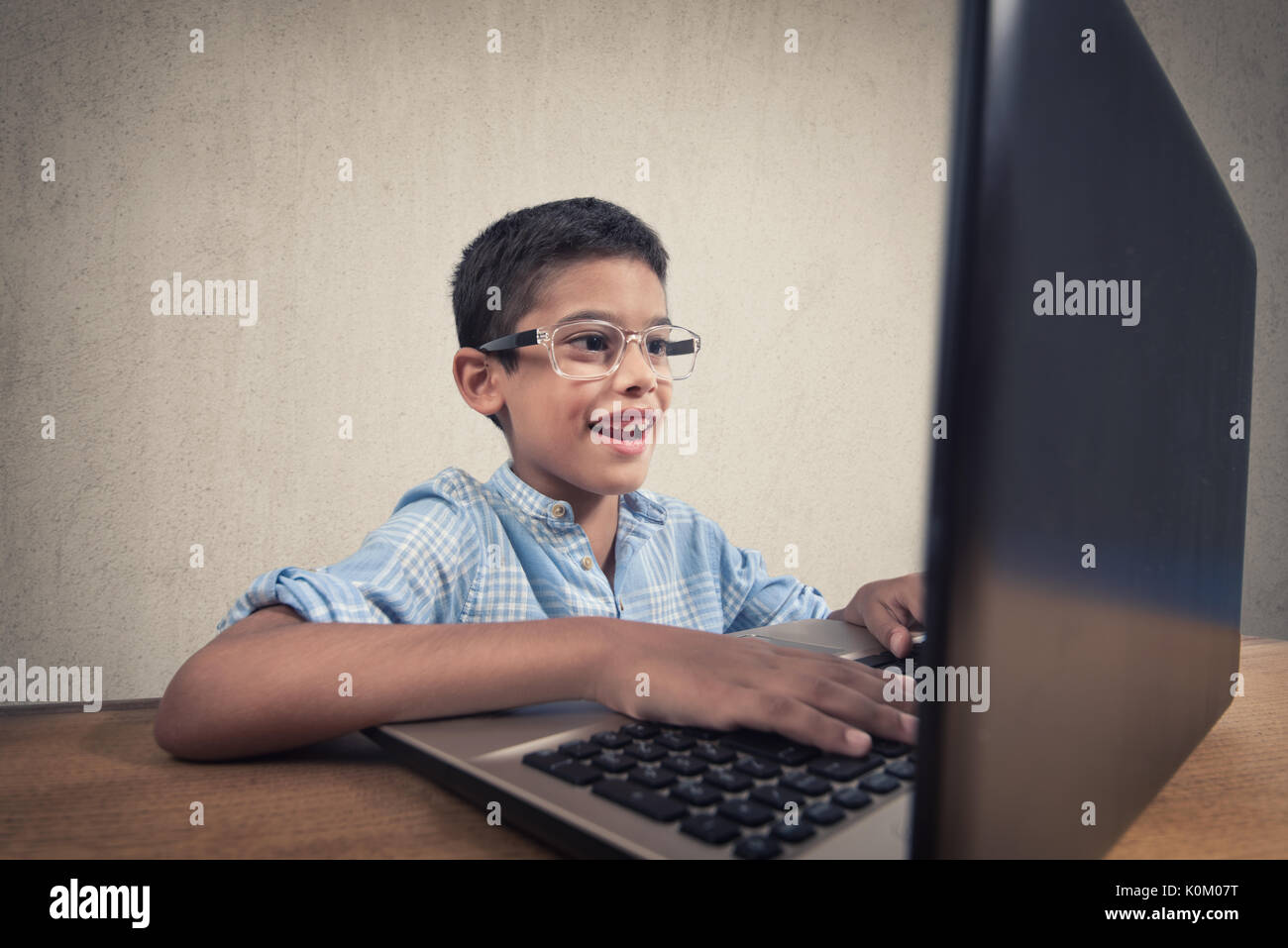 Felice ragazzo seduto alla sua scrivania con computer portatile Foto Stock