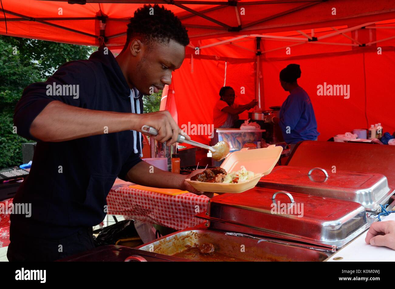 Uomo che serve cibo caraibico ad una street food festival Swansea Food Festival Galles Cymru REGNO UNITO GB Foto Stock
