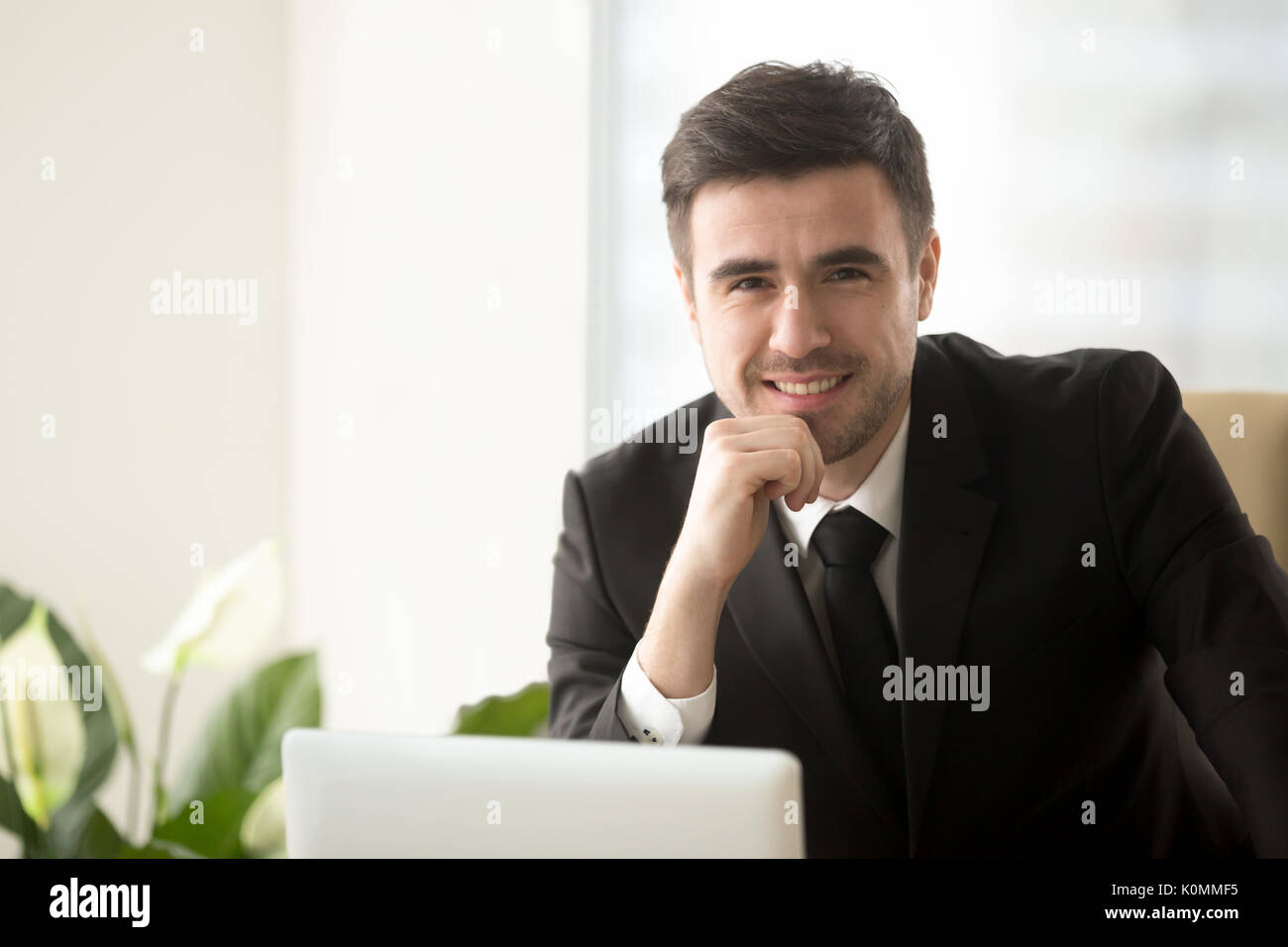 Sorridente attraente uomo d affari con computer portatile guardando alla fotocamera, egli Foto Stock