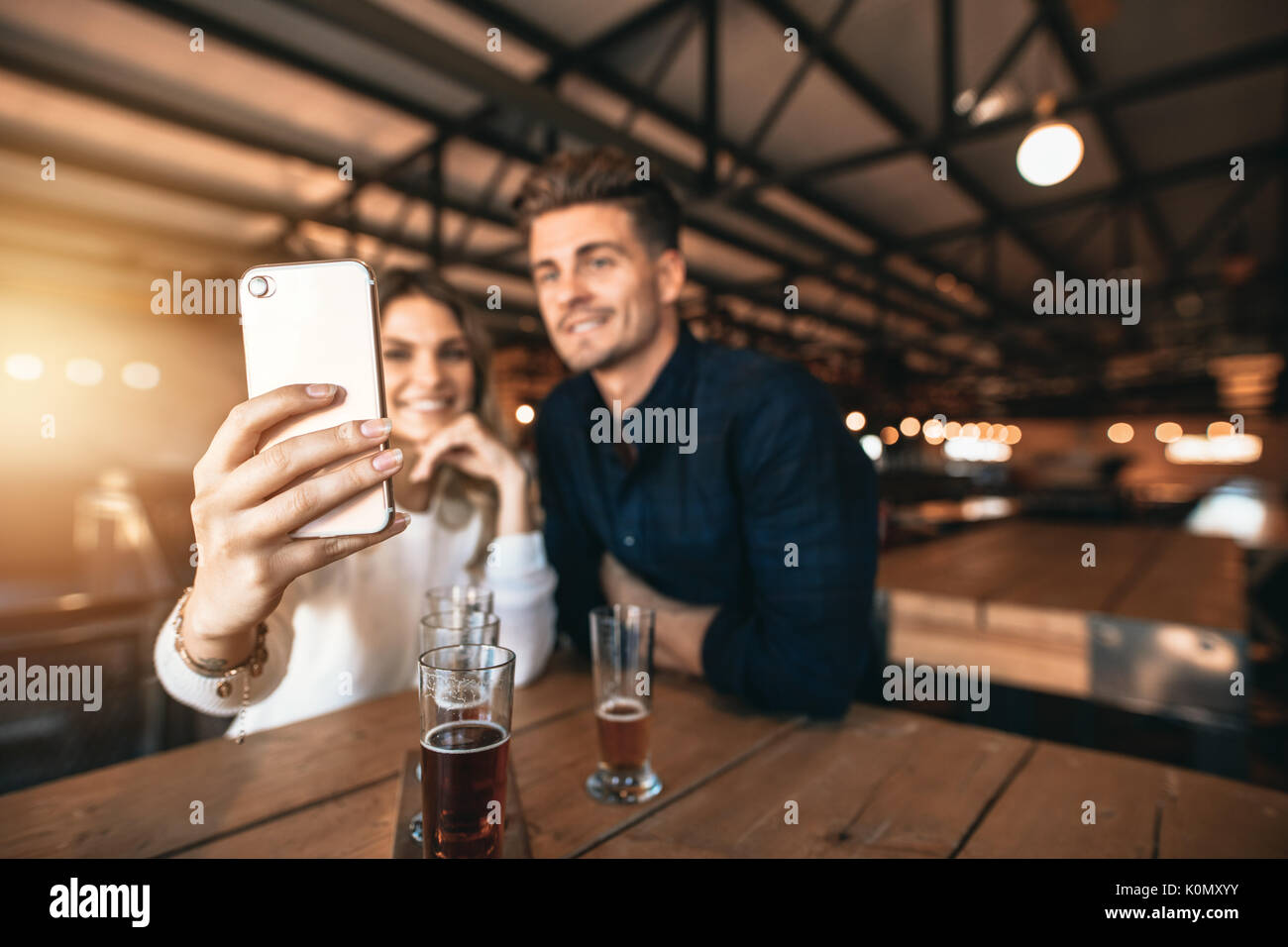 Coppia giovane seduto al bar e prendendo un selfie con il telefono cellulare. Focus su smart phone in mano di donna. Foto Stock