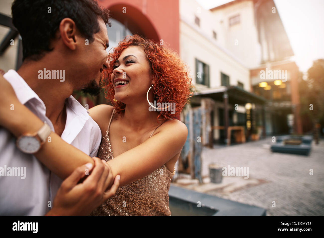 Donna che mantiene il suo partner con le braccia intorno alla ricerca nei suoi occhi. Coppia giovane trascorrendo momenti romantici fuori in strada. Foto Stock