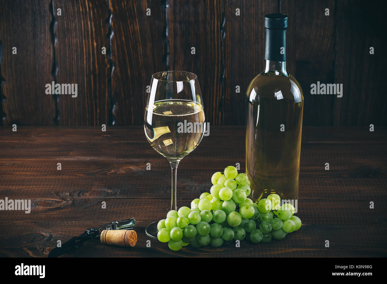Splendido vino bianco in vetro del vino con un grappolo di uva verde, su uno sfondo di legno con spazio libero Foto Stock