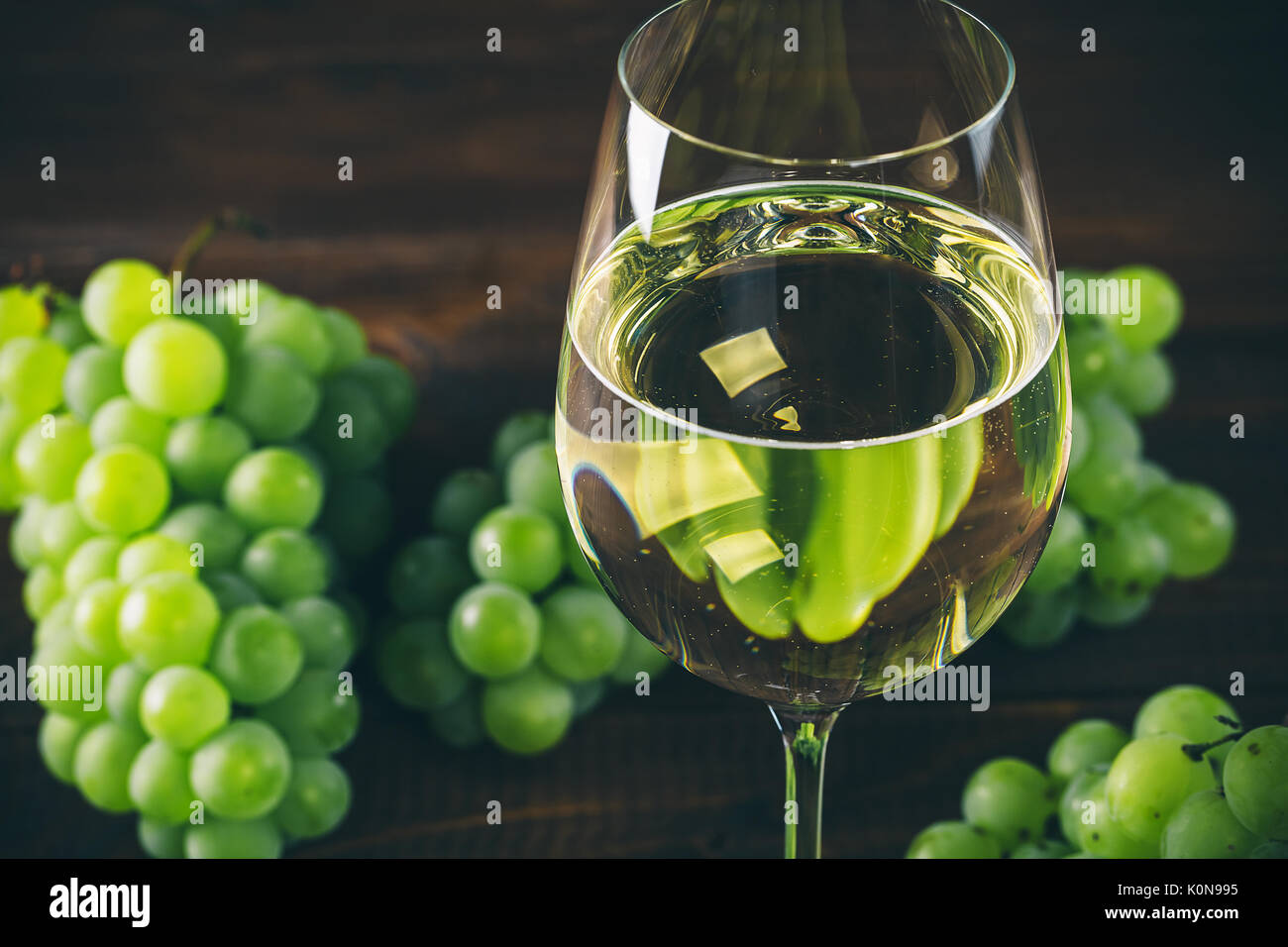 Vino bianco pieno in bicchieri di vino con un grappolo di uva verde, su uno sfondo di legno Foto Stock