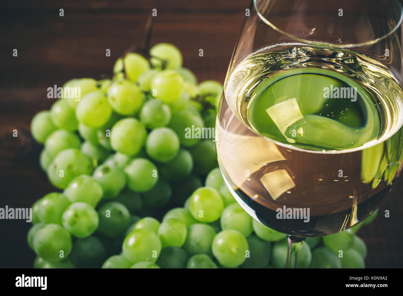 Vino bianco pieno in bicchieri di vino con un grappolo di uva verde, su uno sfondo di legno Foto Stock