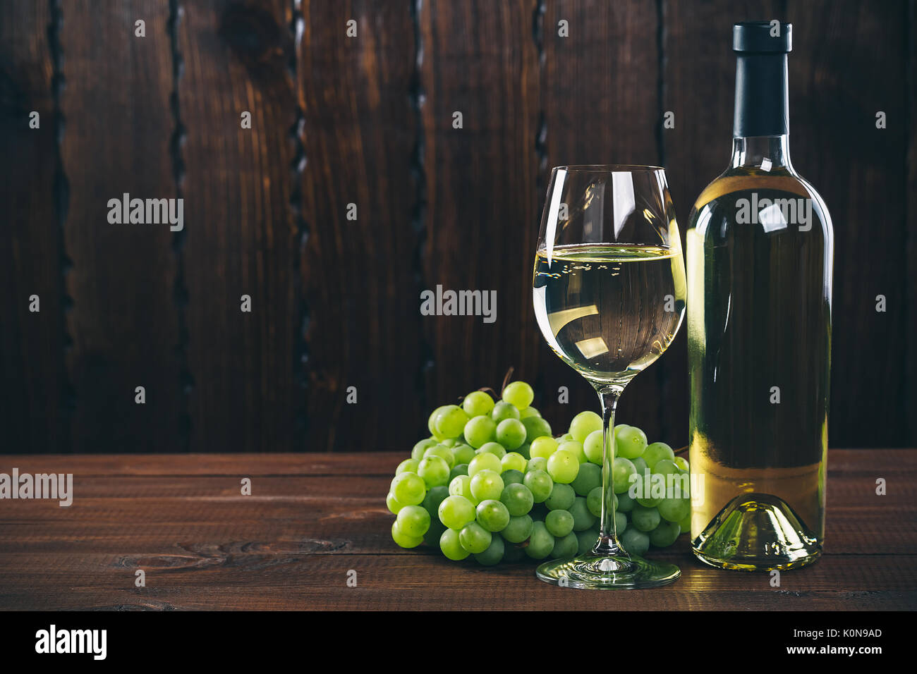 Splendido vino bianco in vetro del vino con un grappolo di uva verde, su uno sfondo di legno con spazio libero Foto Stock