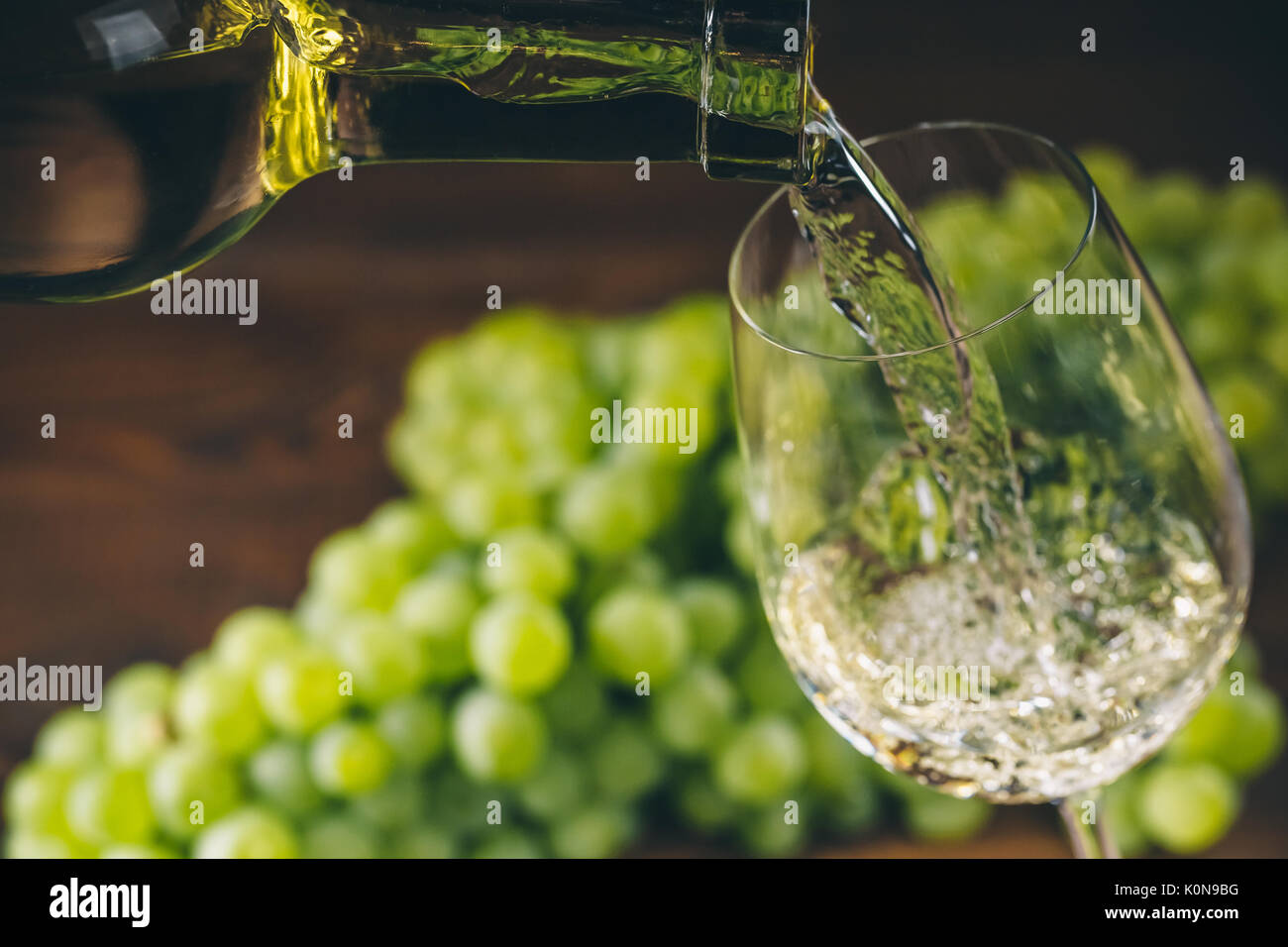 Versare il vino bianco in un bicchiere con un grappolo di uva verde contro lo sfondo di legno Foto Stock