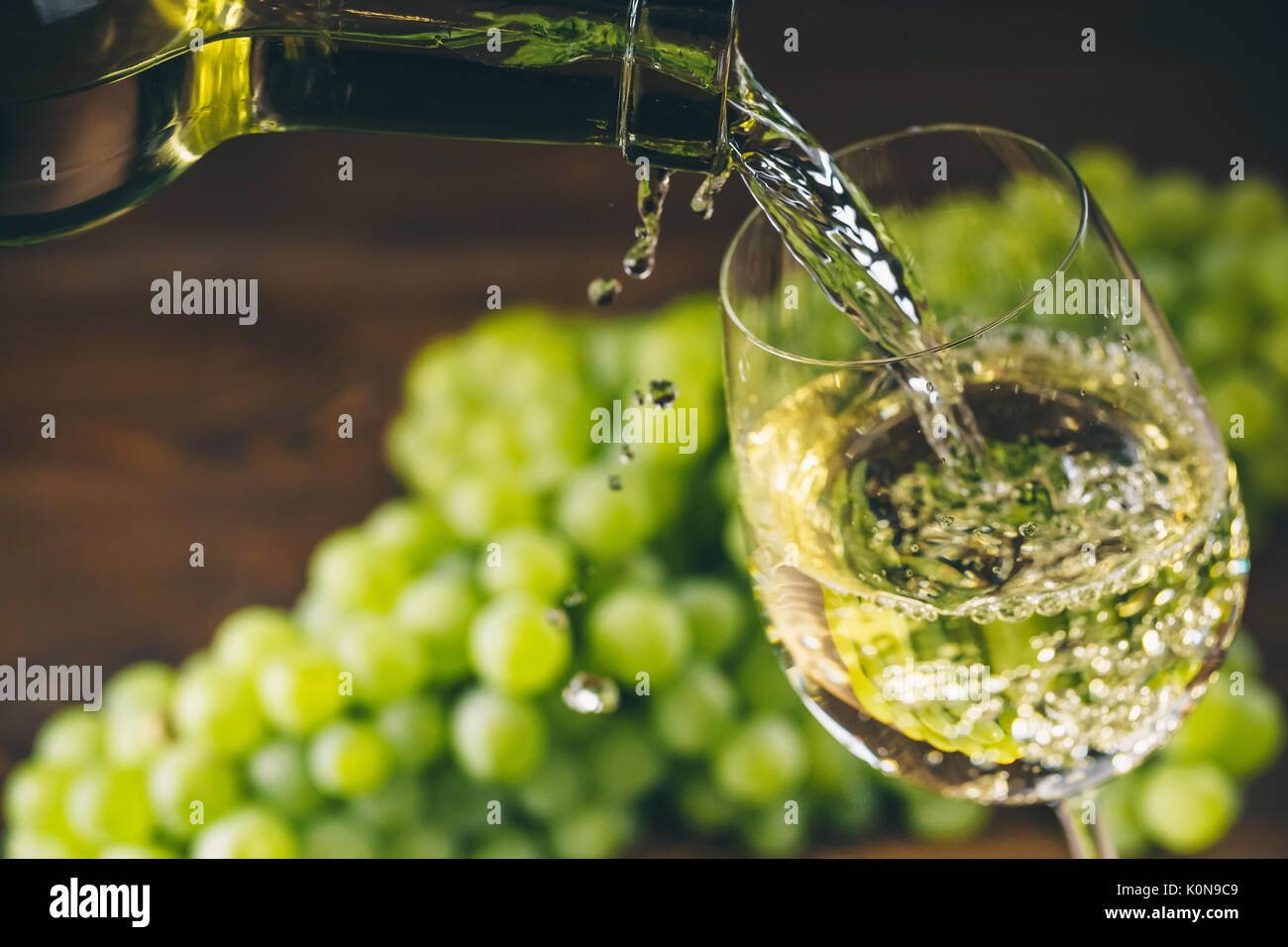 Versare il vino bianco in un bicchiere con un grappolo di uva verde contro lo sfondo di legno Foto Stock