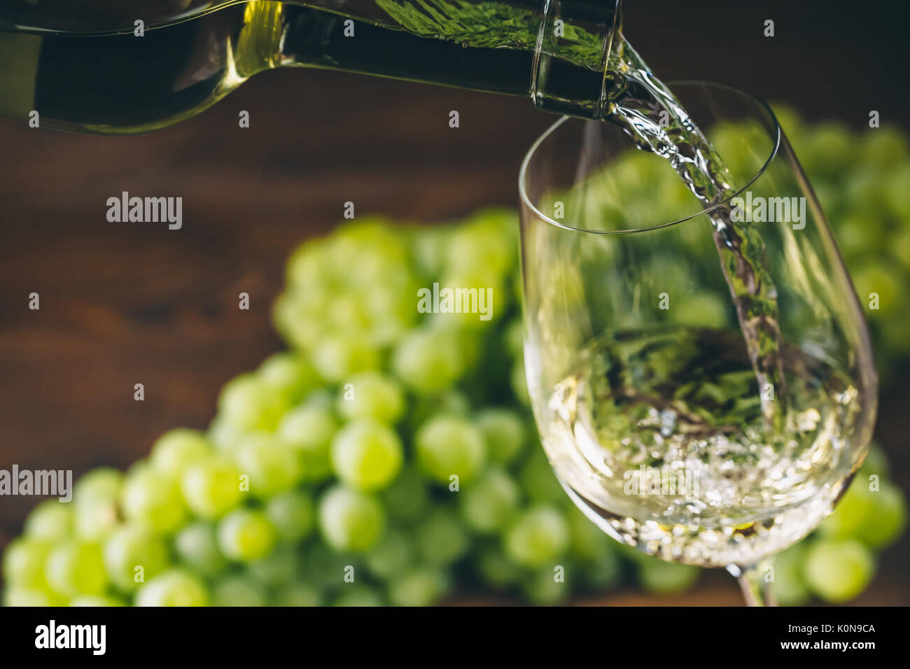 Versare il vino bianco in un bicchiere con un grappolo di uva verde contro lo sfondo di legno Foto Stock