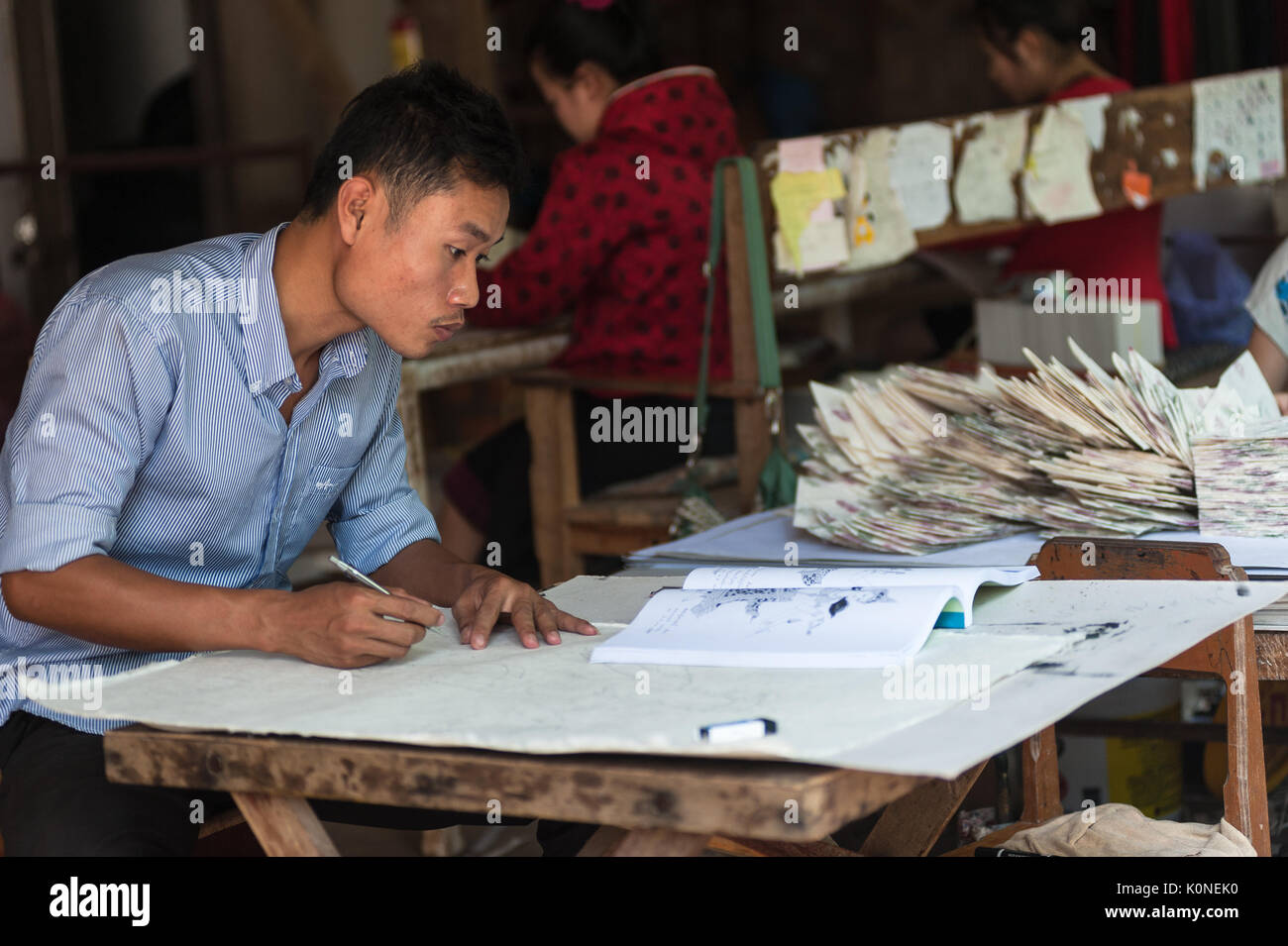 Un giovane illustratore riproduce le figure su un tradizionale "aa' carta fatta nel locale di studio in Xhang Khong village vicino a Luang Prabang, Laos. Foto Stock