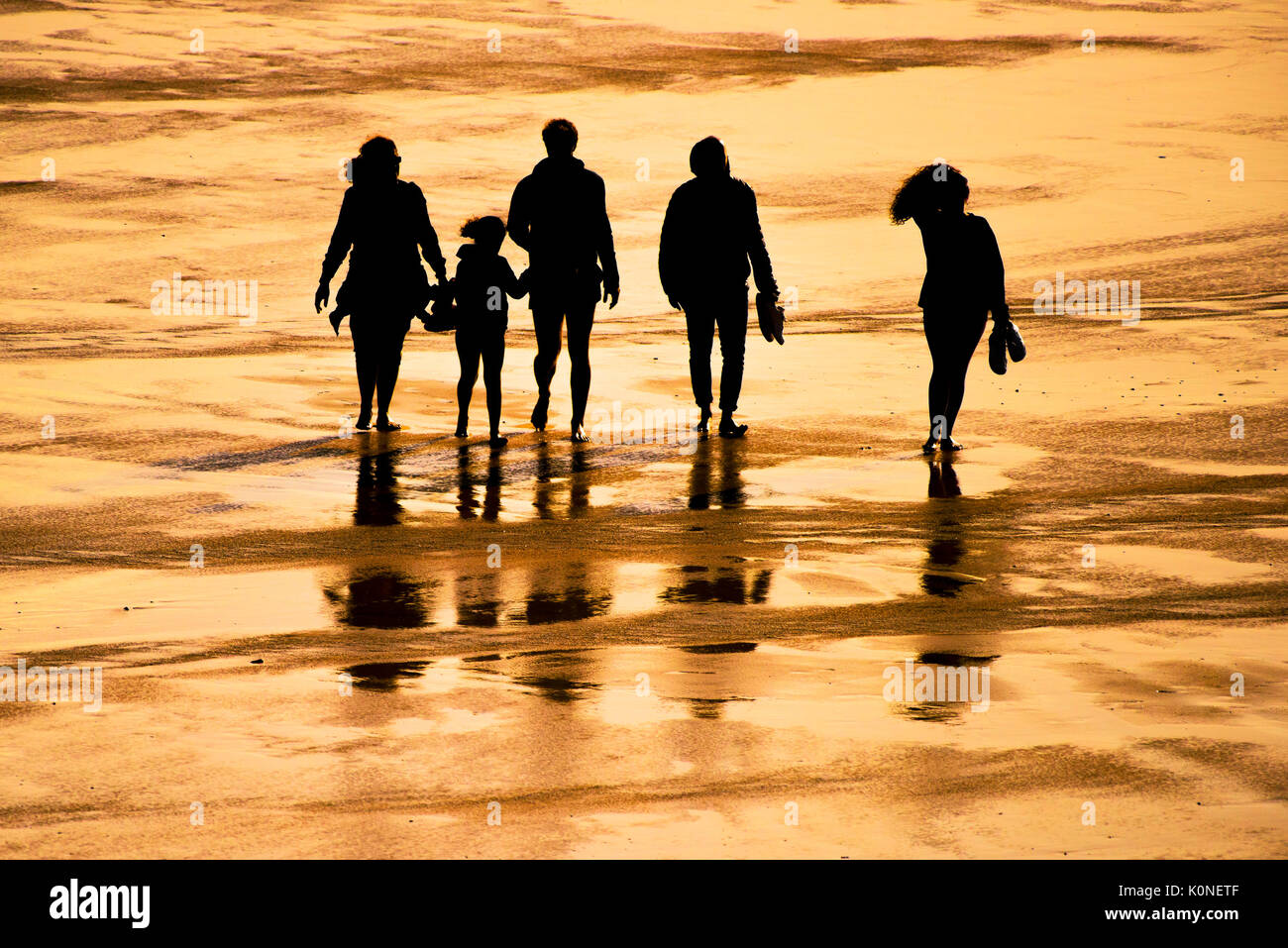 La silhouette di una famiglia di vacanzieri a camminare su una spiaggia al tramonto. Foto Stock