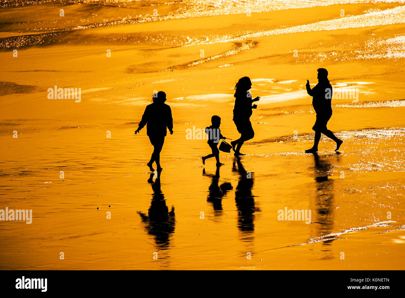 La silhouette di una famiglia di vacanzieri che si diverte sulla spiaggia al tramonto. Foto Stock