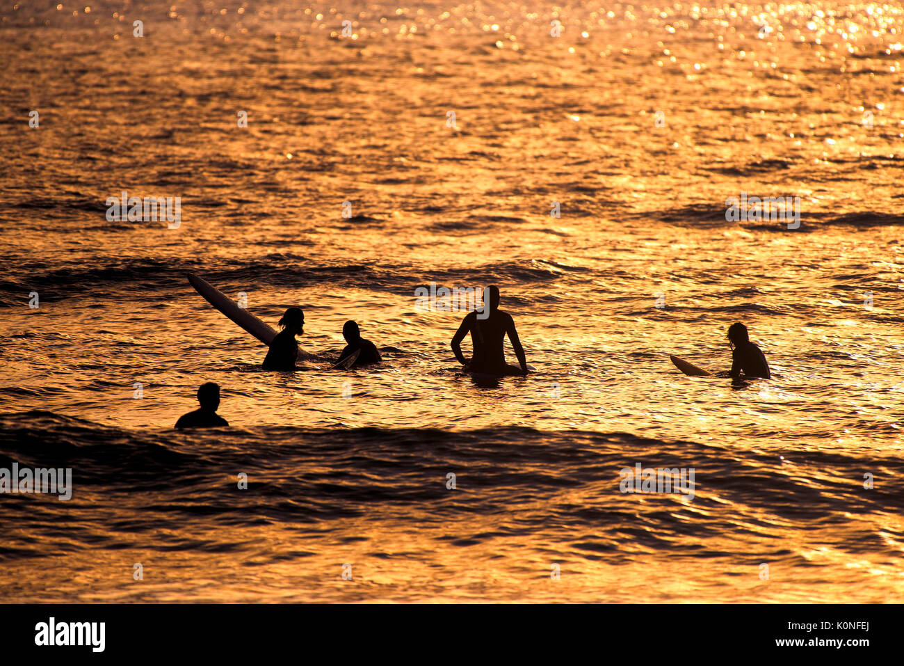 La silhouette di surfers in attesa di un'onda durante un intenso tramonto a Fistral in Newquay. Foto Stock
