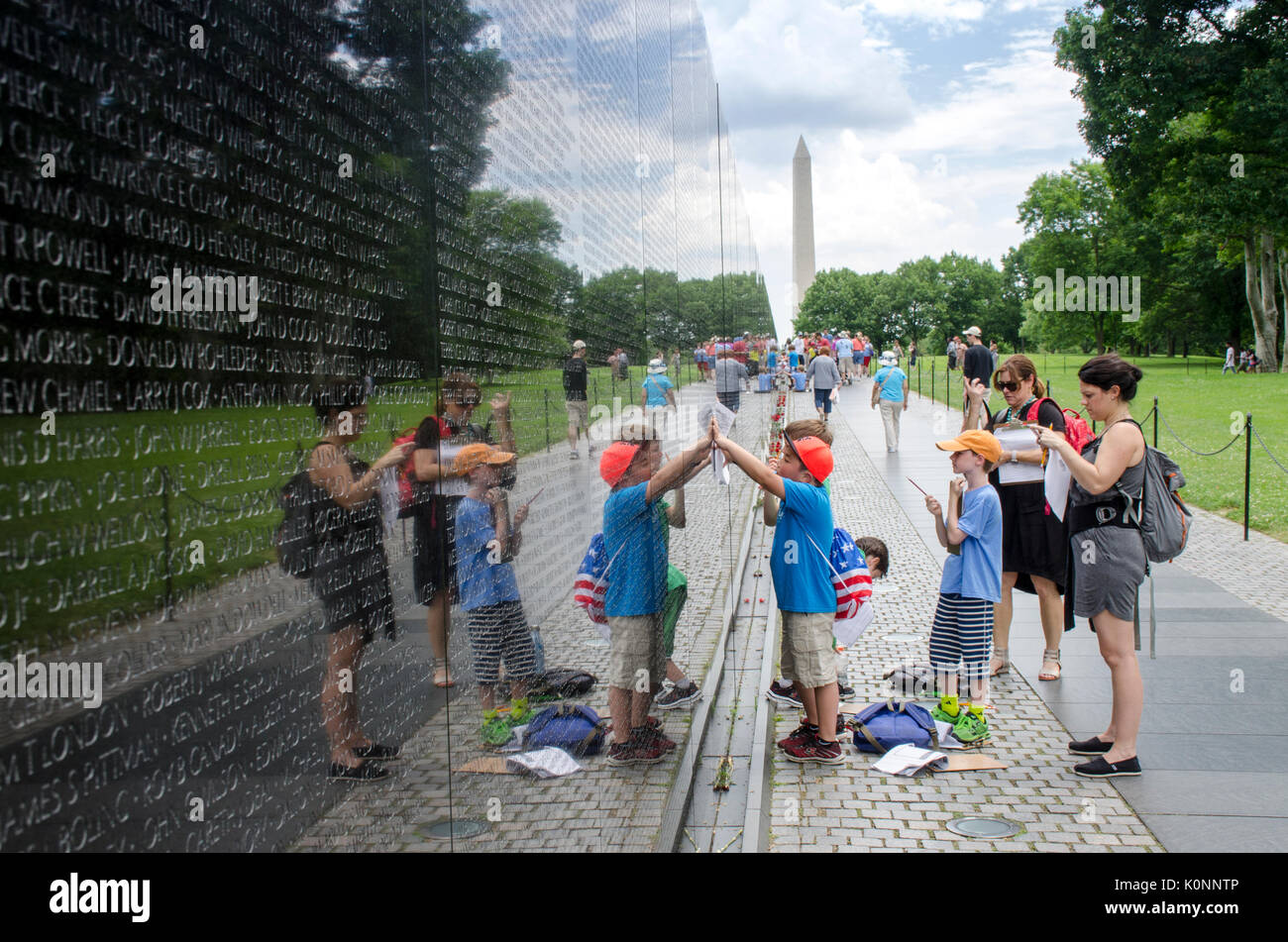 La scuola dei bambini, con l'aiuto del loro maestro, a matita di strisciamenti dei nomi sul Vietnam Veterans Memorial wall. Il Monumento a Washington è di Foto Stock