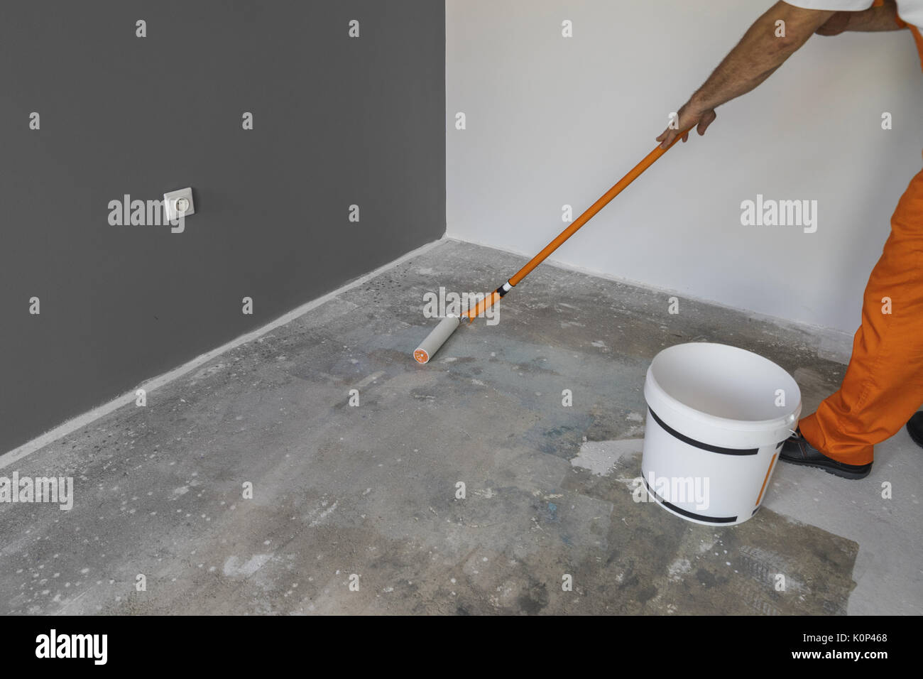 La mano di un uomo con un rullo e mette la pompetta di adescamento sul pavimento di cemento Foto Stock