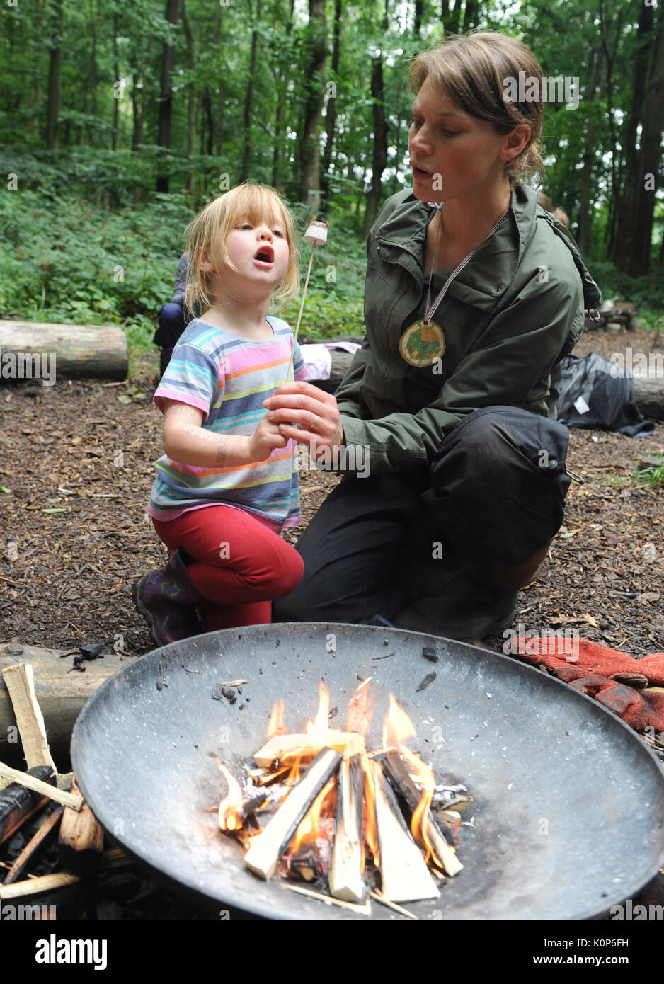 Donna e bambina tostare un marshmallow oltre a una buca per il fuoco in una scuola della foresta Foto Stock