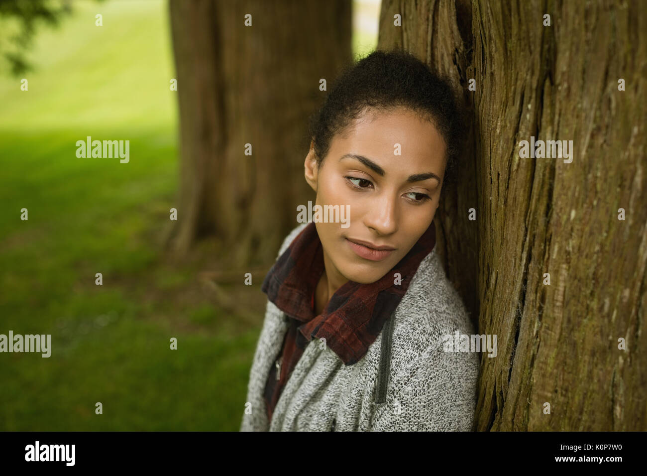 Close-up di pensosa donna appoggiata sul tronco di albero Foto Stock
