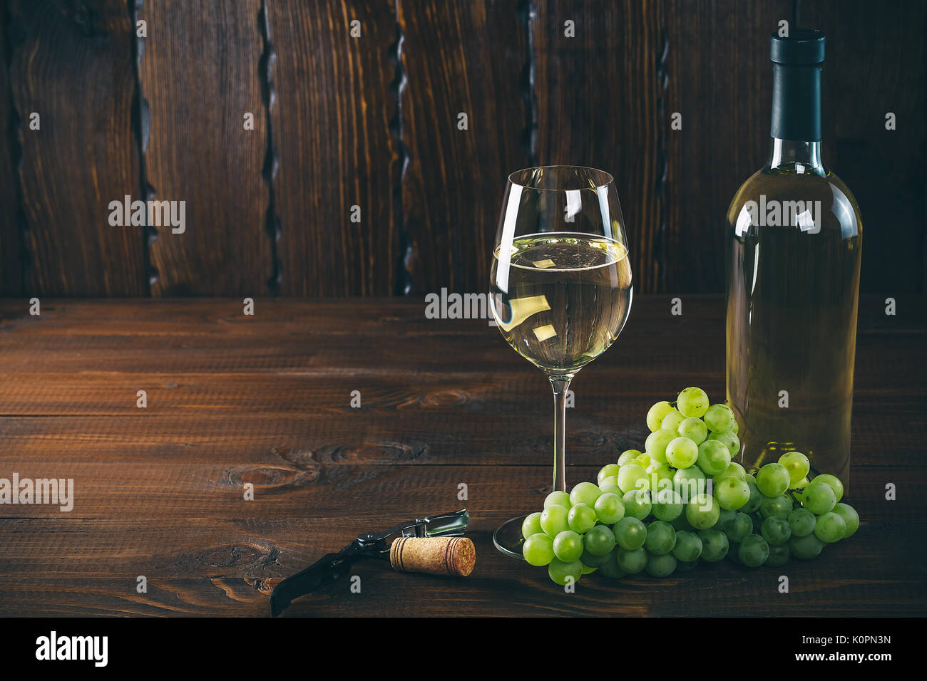 Splendido vino bianco in vetro del vino con un grappolo di uva verde, su uno sfondo di legno con spazio libero Foto Stock