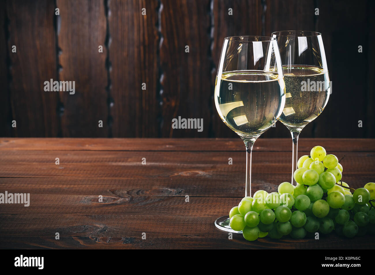 Splendido vino bianco in vetro del vino con un grappolo di uva verde, su uno sfondo di legno con spazio libero Foto Stock