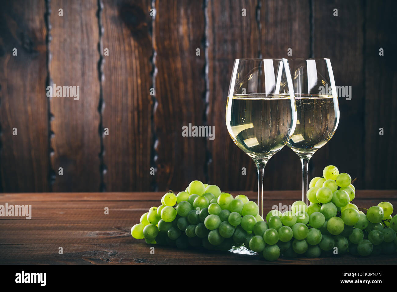 Splendido vino bianco in vetro del vino con un grappolo di uva verde, su uno sfondo di legno con spazio libero Foto Stock